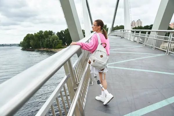 stock image A spirited young woman embraces fitness outdoors, confidently walking on a scenic bridge.