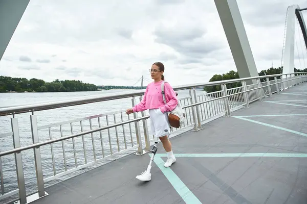 stock image A young woman confidently walking outdoors, showcasing her prosthetic leg while enjoying the fresh air.