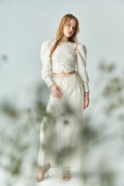 Güzel bir kadın, sakin bir ortamda çiçek aksanıyla süslenmiş zarif bir şekilde ayakta duruyor..