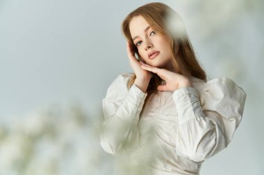 Genç bir kadın narin çiçeklerin arasında nazikçe poz verir, ışıldayan güzellik ve zarafet.