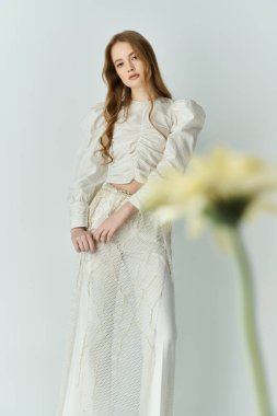 Genç bir kadın zarif, canlı çiçeklerle çevrili, ışıl ışıl bir cazibeyle ayakta duruyor..