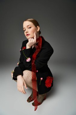 Genç bir kadın şık bir elbise içinde çiçeklerle süslenmişken zarif poz verir..