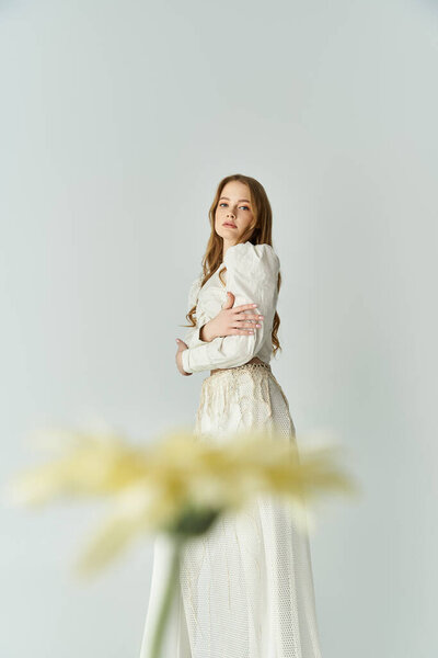 Молодая женщина держит цветы, олицетворяющие грацию и красоту в мягкой, яркой атмосфере.