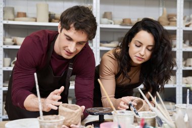 A couple joyfully shapes clay in a contemporary pottery studio. clipart