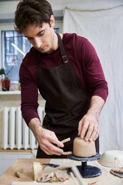 Attractive male in apron making some pottery in studio. clipart