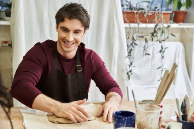 Young man in apron making some pottery and smiling happily. clipart