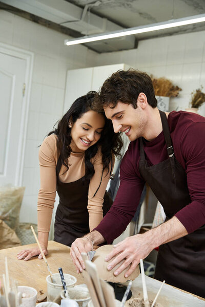 Two people share smiles while shaping clay in a creative space.
