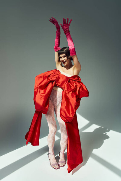 A cheerful young woman strikes a playful pose in a striking red dress.