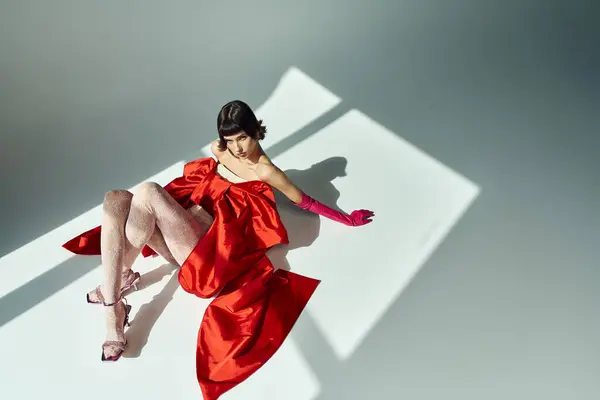 Stock image A young woman showcases elegance in a vibrant red dress with an oversized bow.