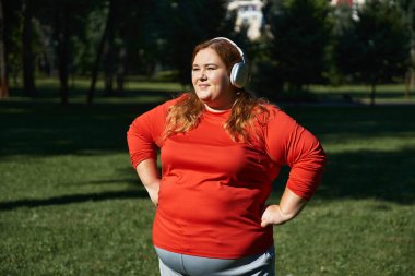 A joyful woman exercises outdoors, embracing her fitness journey with headphones on. clipart