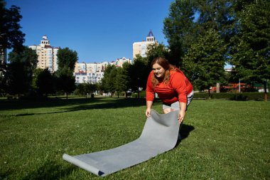 Kararlı bir kadın paspası kaldırır ve yemyeşil parkta egzersiz yapmaya başlar..