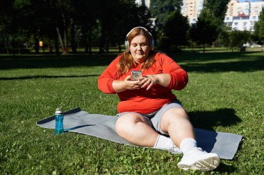 Bir kadın parkta egzersiz yapıyor, telefonuyla meşgul oluyor ve sağlıklı bir yaşam tarzını benimsiyor..