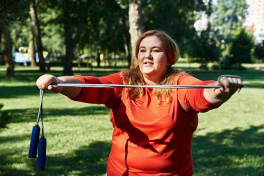 A beautiful woman engages in exercise with a jump rope in the park. clipart