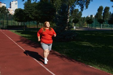 A woman enjoys jogging through a lush park under clear skies. clipart