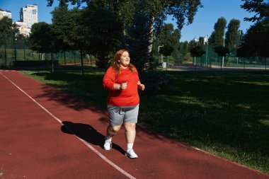 Neşeli bir kadın enerjik bir parkta koşuyor, dışarıda spor yapmayı kutluyor..