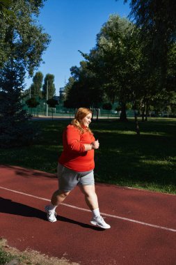 Neşeli, iri yarı bir kadın güneşli parkta dışarıda egzersiz yapıyor..