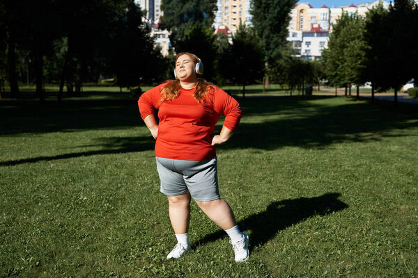 Уверенная в себе женщина plus size упражняется в наушниках в пышном зеленом парке.