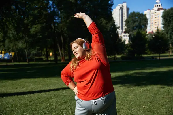 stock image A woman exercises outdoors, stretching her arms under the sun in a green park.