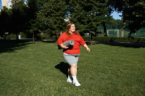 stock image A woman walks confidently in a park with an exercise mat.