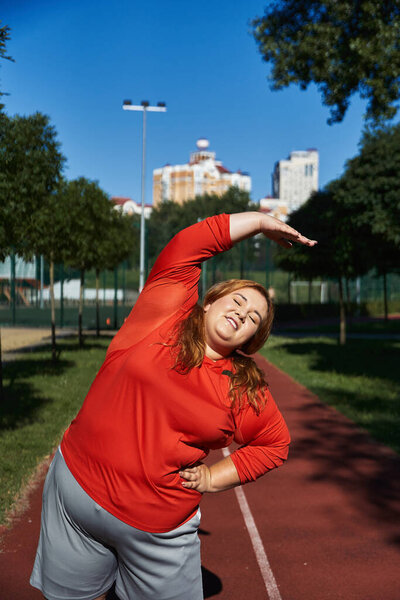 Радостная женщина растягивается в парке, обнимая утреннее солнце.
