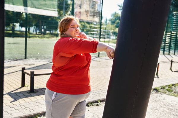 A determined woman engages in exercise, striking a punching bag outdoors.