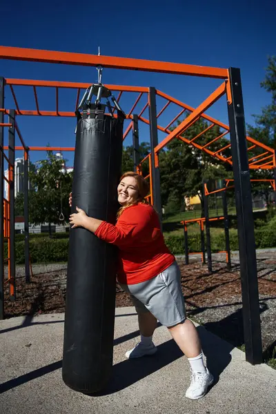 stock image A plus size woman smiles as she exercises at a park on a bright day.