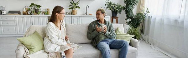 Небинарный человек и его друг расслабляются и общаются в ярком, привлекательном пространстве.