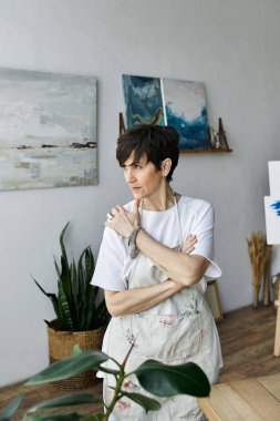 A woman contemplates her artwork in a bright, inspiring studio. clipart