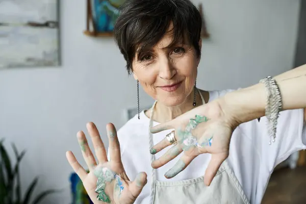 stock image A mature woman joyfully showcases her paint splattered hands while working.