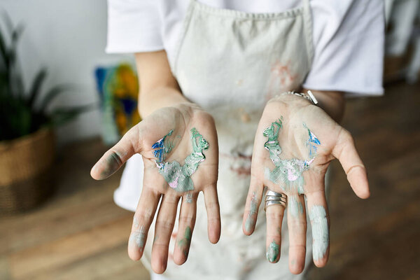 A mature artist with paint splattered hands blends colors happily in her studio.