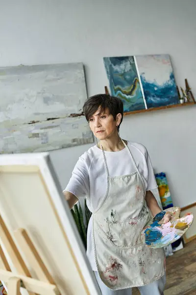 stock image A woman engages in painting with a palette in hand, immersed in her creative space.