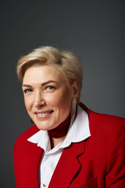 Yetişkin bir kadın, kendine güveni tam bir gülümseme sergileyen çarpıcı kırmızı kıyafetiyle zarafet saçar..