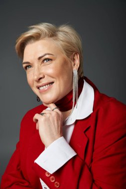Kırmızı şık bir kıyafet giyen yetişkin bir kadın sıcak bir şekilde gülümserken kendine güvenir..