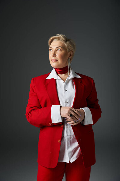 An elegant adult woman in a striking red suit exudes confidence in a minimalist setting.