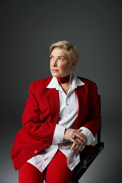 Стильная взрослая женщина в шикарном красном наряде сидит элегантно, излучая уверенность и изящество.