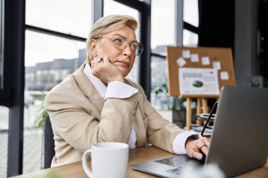 Modaya uygun bir kadın, çağdaş ofis masasında çalışırken yansıtır..