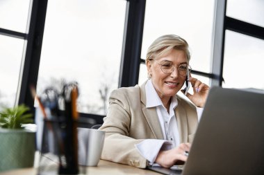 Yetişkin bir kadın, dizüstü bilgisayarı üzerinde çalışırken zarif bir şekilde bir telefon görüşmesi yapar..