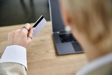 Şık giyinmiş yetişkin bir kadın internetten alışveriş yapmaya hazırlanırken elinde bir kart tutuyor..