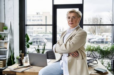 Yetişkin bir kadın, çalışma alanında dururken sofistike moda anlayışını sergiliyor..