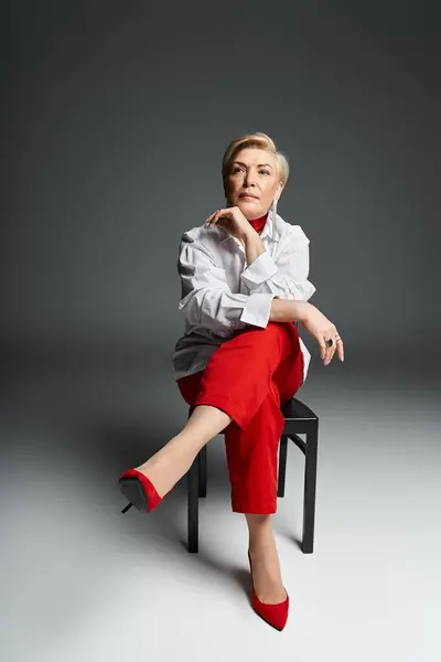 stock image A fashionable woman dressed in vibrant red exudes confidence while seated, showcasing her elegance.