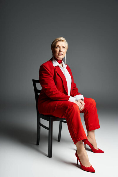 An elegantly dressed woman in vibrant red attire sits poised, exuding confidence and style.