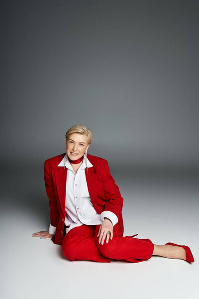 Уверенная в себе женщина в ярком красном костюме позирует с уравновешенностью, демонстрируя свое чувство стиля и обаяние.