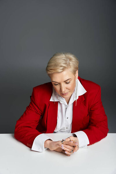 Уравновешенная женщина, одетая в элегантный красный наряд, спокойно созерцает гладкий стол.