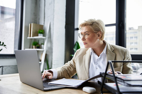 Элегантная женщина, одетая стильно, фокусируется на своей работе за современным столом в ярком пространстве..