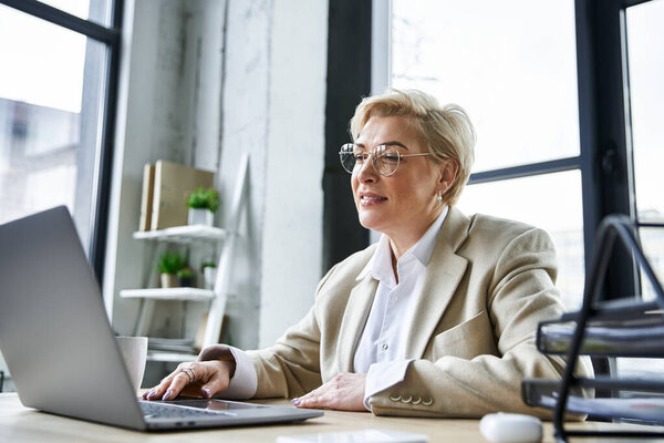 An adult stylish woman engages with her laptop, showcasing elegance in a contemporary workspace.