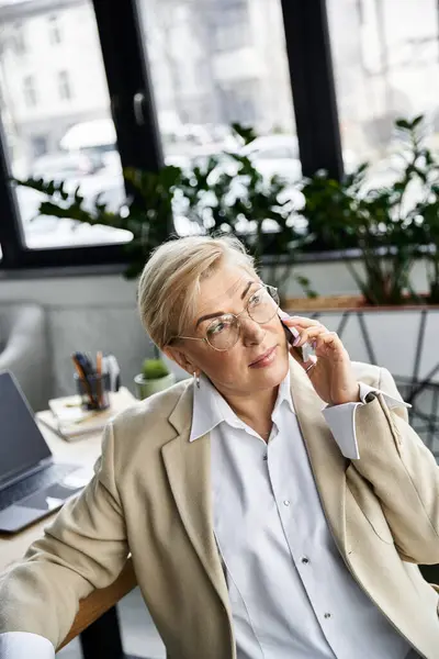 stock image An elegant woman engages in a phone conversation while seated in a chic office environment.