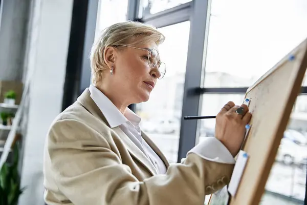 stock image A sophisticated woman in elegant clothing intently draws on a large board, showcasing creativity.