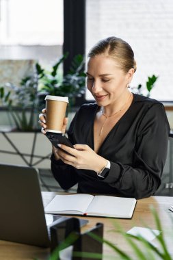 İşteki iri yarı genç bir kadın, kahvesini yudumluyor ve parlak bir ofiste telefonunu kullanıyor..