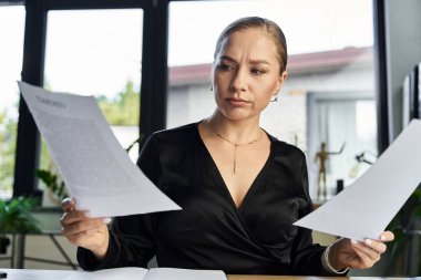 A plus size woman with a focused expression is evaluating paperwork at her desk. clipart