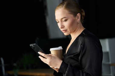 Genç, güzel, iri yarı bir kadın, elinde kahve olan akıllı telefonuyla bir ofiste meşgul..